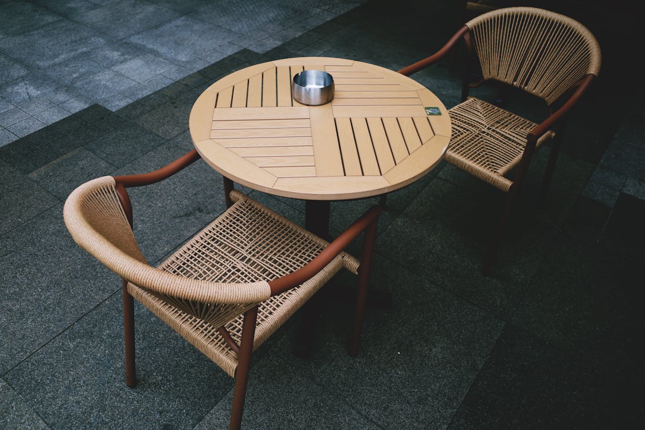 Stylish wooden table and woven rattan chairs on a stone patio, perfect for outdoor dining.