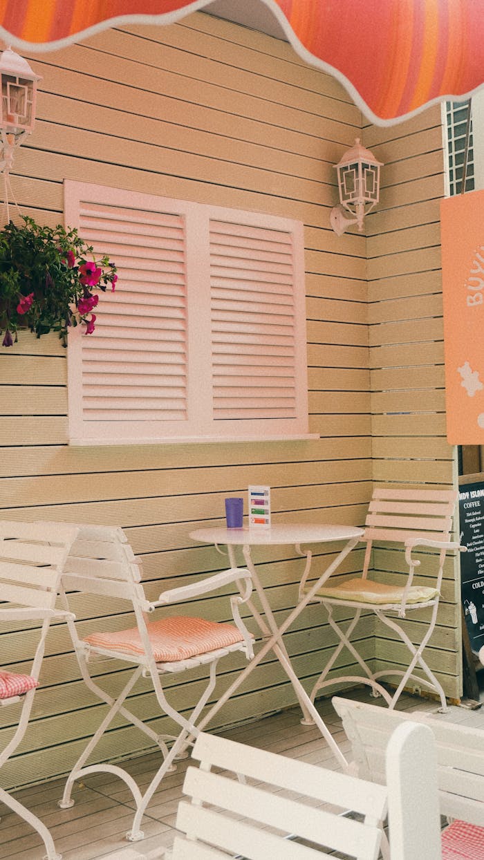 Charming outdoor patio setting with white furniture and pink accents, perfect for relaxation.